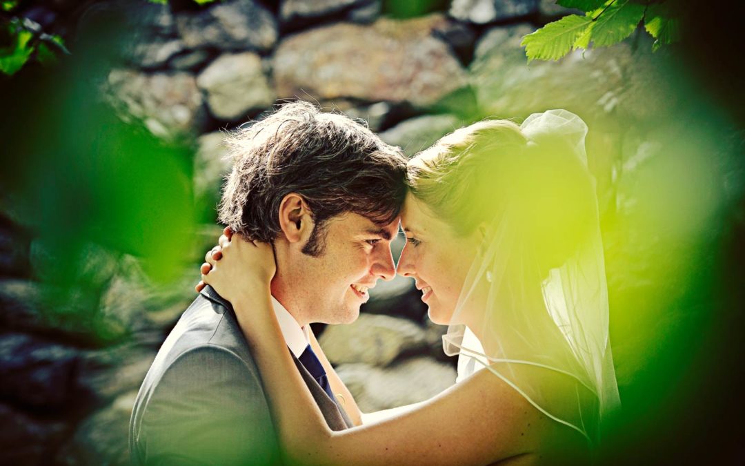 Bröllopsfoto från Marstrand. Par framför mur med löv i förgrunden.
